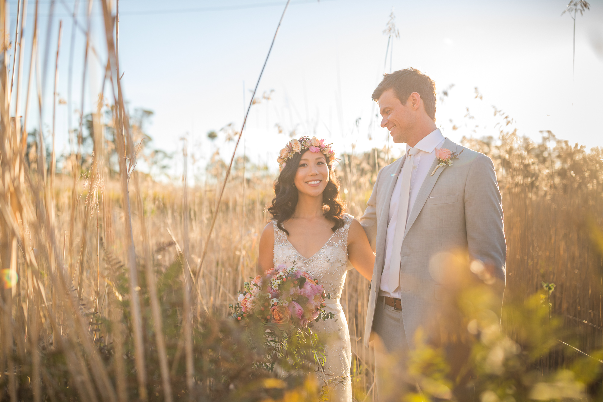 Smiling newlyweds standing in a field with soft light and romantic colours