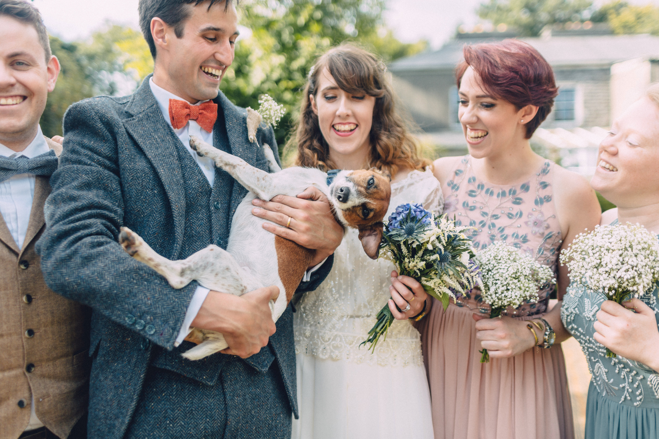 Newly weds holding a dog while bridal party smiles