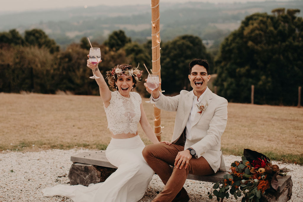 married couple toasting drinks while sitting on  bench for boho wedding inspiration