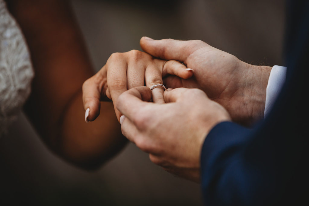 Groom places diamond ring on bride's finger. 