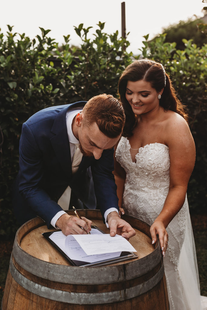 what getting married feels like: Couple sign marriage paperwork on a barrell with huge smile on face