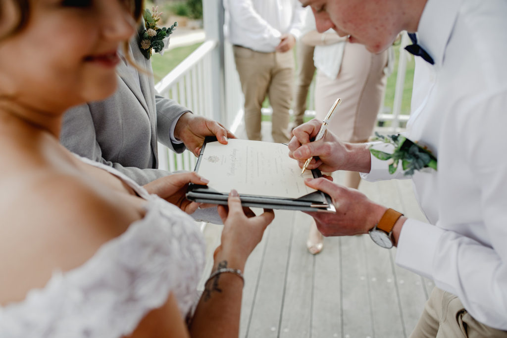 Couple sign the marriage paperwork on the balcony of one of the rooms out of the rain at Caves Coastal Bar & Bungalows