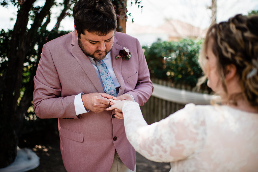 Groom slides ring onto bride's finger during New Lambton wedding.