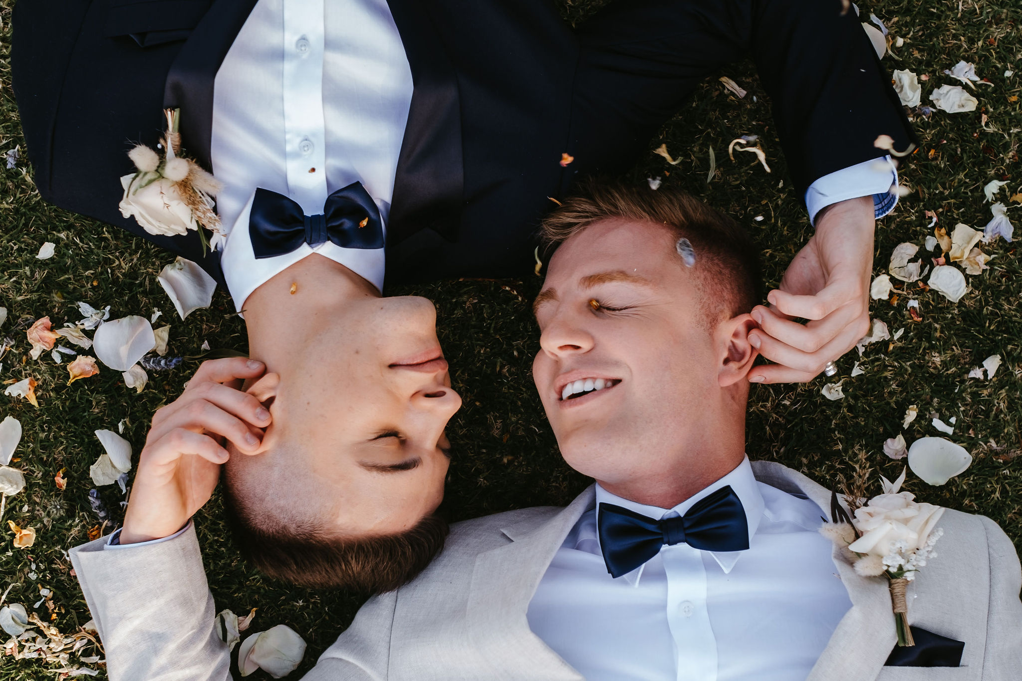 grooms lying on the ground with eyes closed and facing each other
