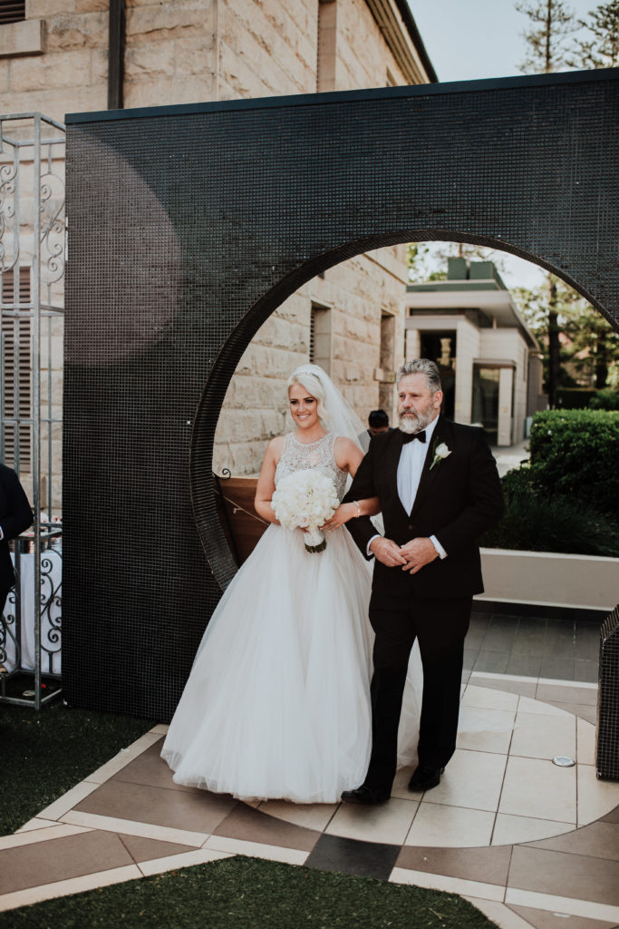 Bride walking through black arch with father at Curzon Hall.