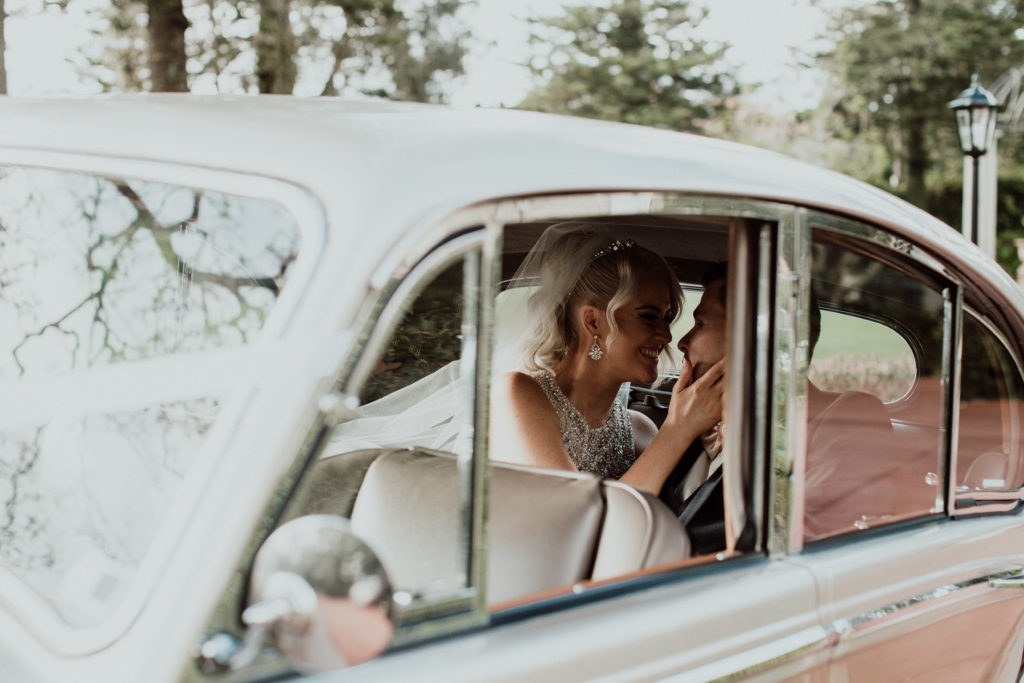 Bride and groom smiling close to each other in a vintage car at Curzon Hall wedding