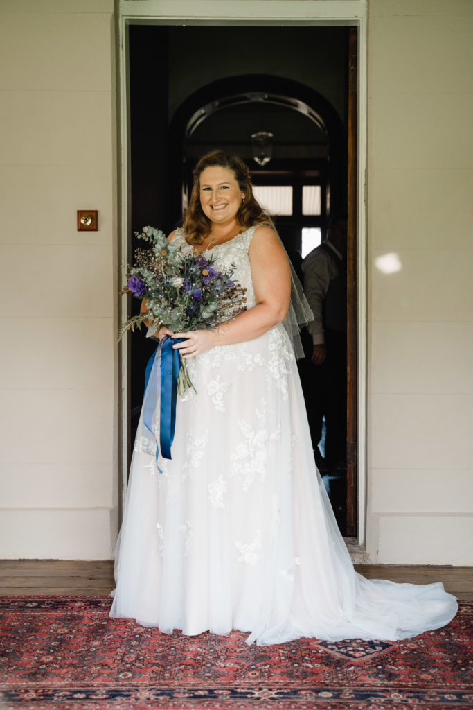 Bride standing at front door of Wallalong House with bouquet in her hands