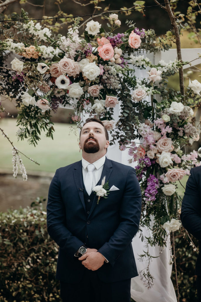 Groom waiting for his bride in front of a flower-decorated wedding arbour