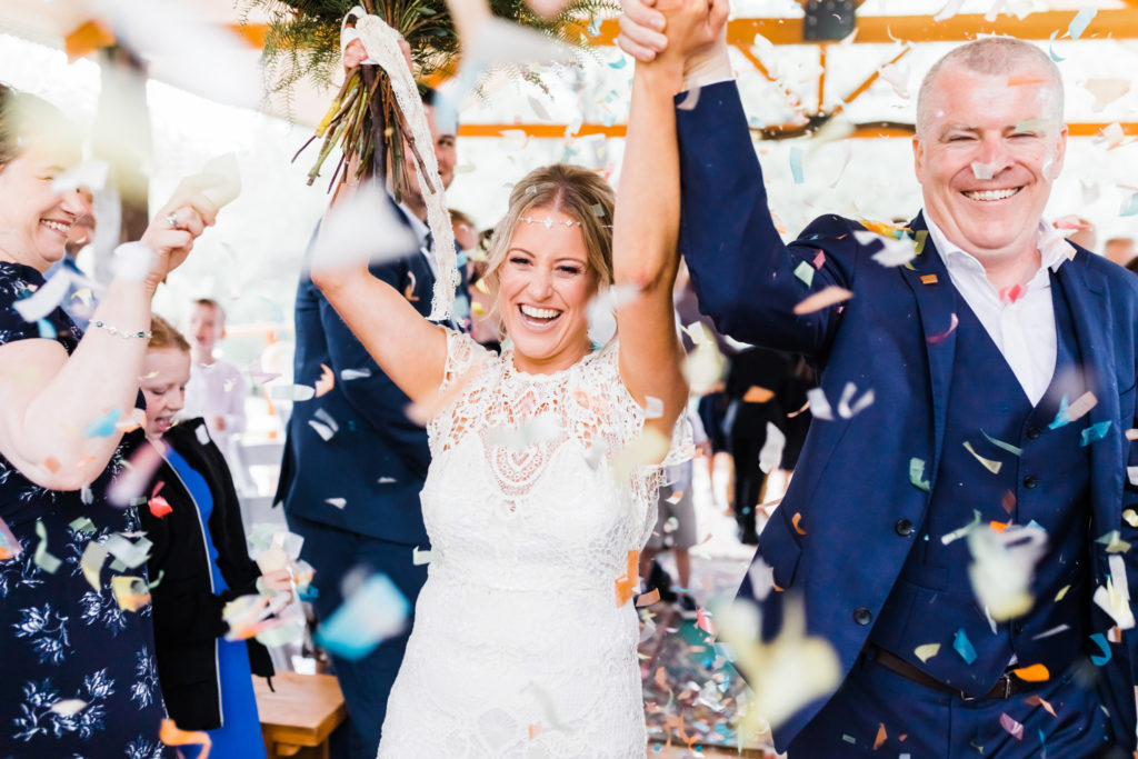 Bride and groom showered in confetti as they walk down the aisle with their hands up