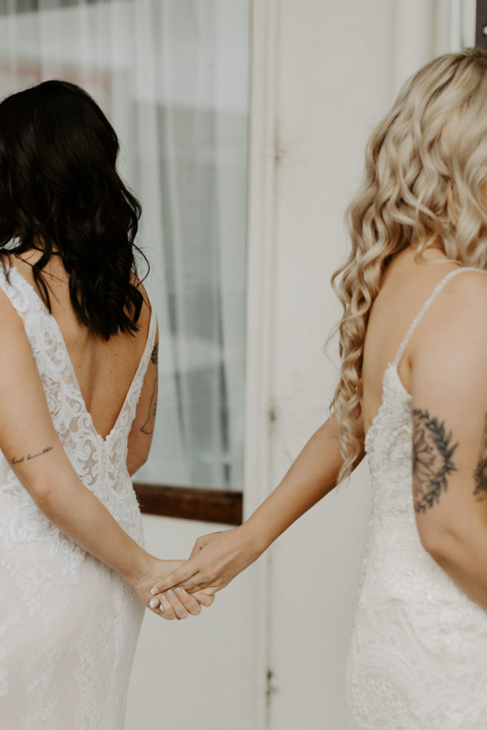 Wedding Social Co brides holding hands from behind for their first look
