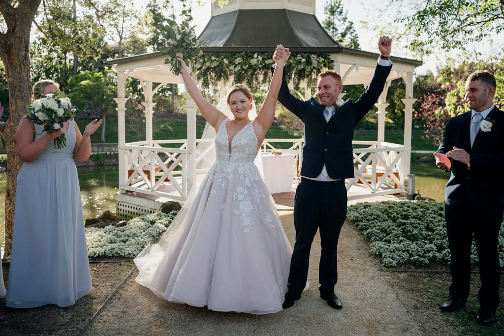 Hunter Valley Gardens wedding newlyweds with their hands up and bridal party clapping around them