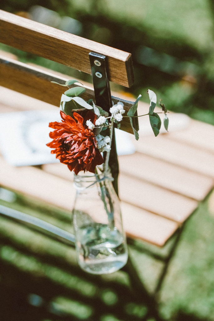 Flower in a clear bottle hanging at the edge of a wooden bench