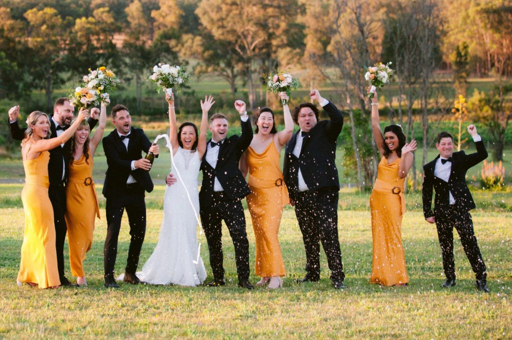 Newlyweds with bridal party popping champagne and raising their hands up at Willow Tree Estate wedding