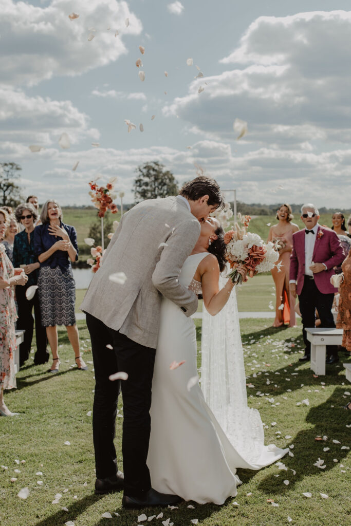 Newlywed couples stopping for a kiss mid-aisle while getting showered with flower confetti