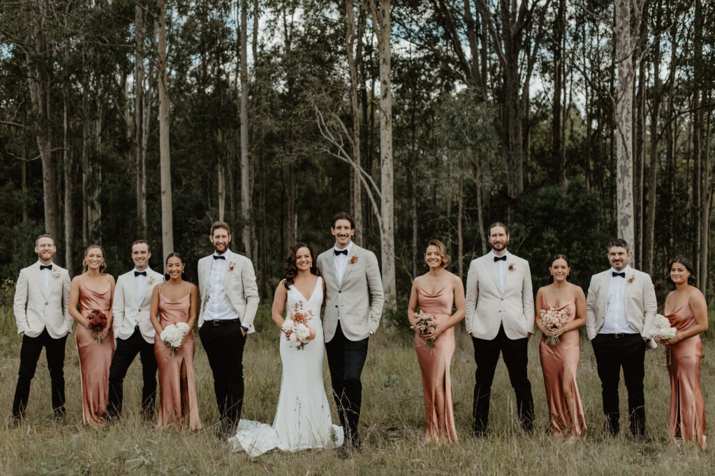 Bridal party standing in pairs in front of woodland