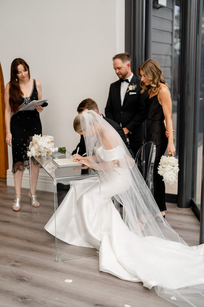 Couple signing their marriage paperwork with celebrant Julie Muir on a glass table