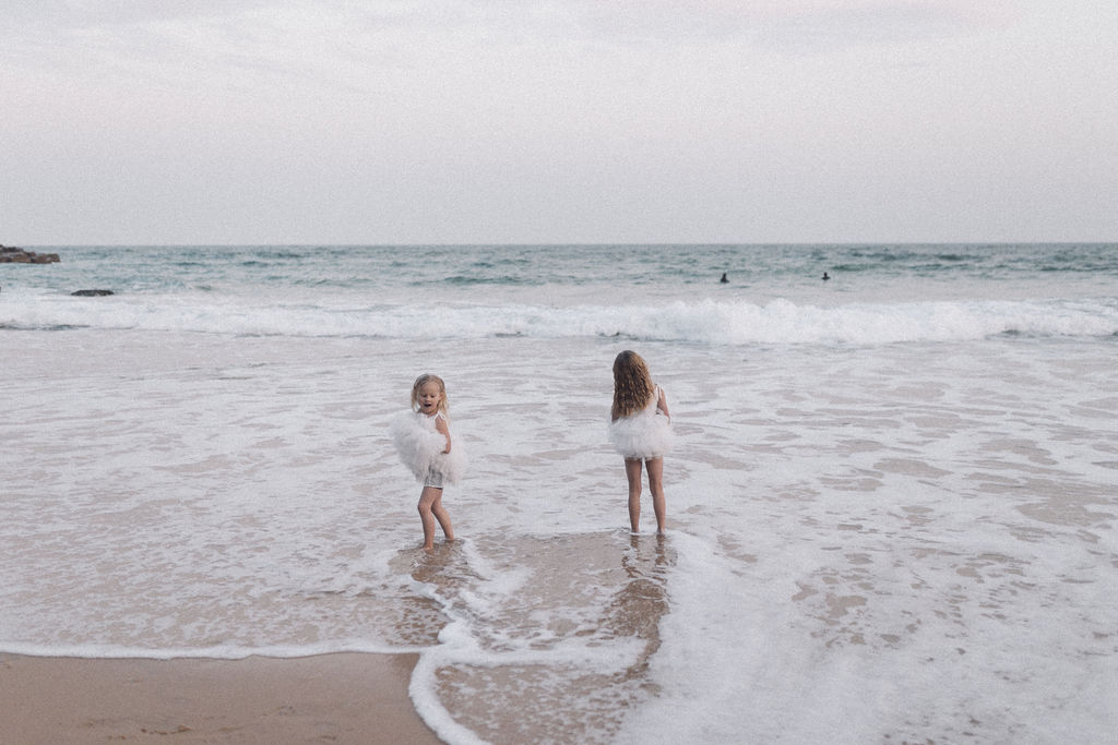 Young girls in white tutu dresses paddling in the ocean at Bar Beach