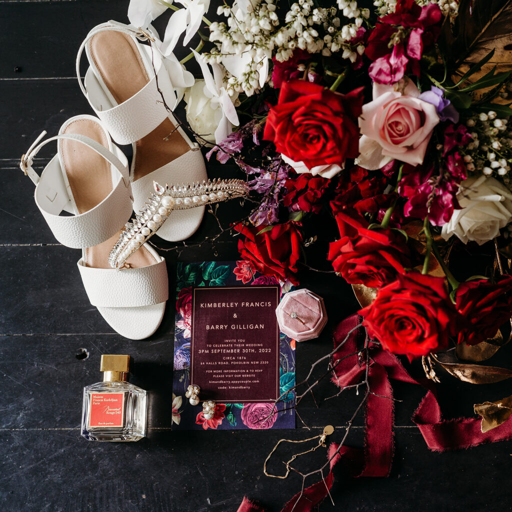 Flat lay showing bride's shoes, bouquet, wedding invitation, wedding ring, and perfume