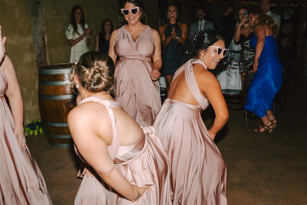 Three bridesmaids wearing white heart sunglasses and dancing at Peppers Creek Chapel & Barrell Room.
