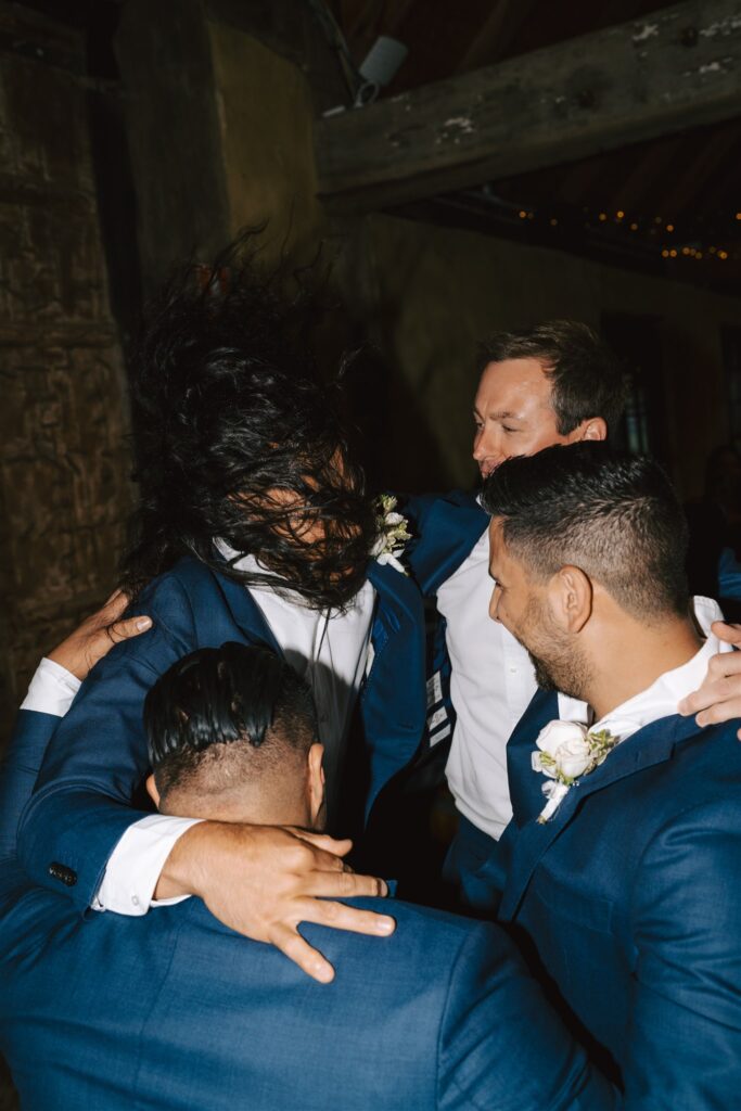Five groomsmen forming a circle with their arms on their shoulders, partying at Peppers Creek Chapel & Barrell Room.