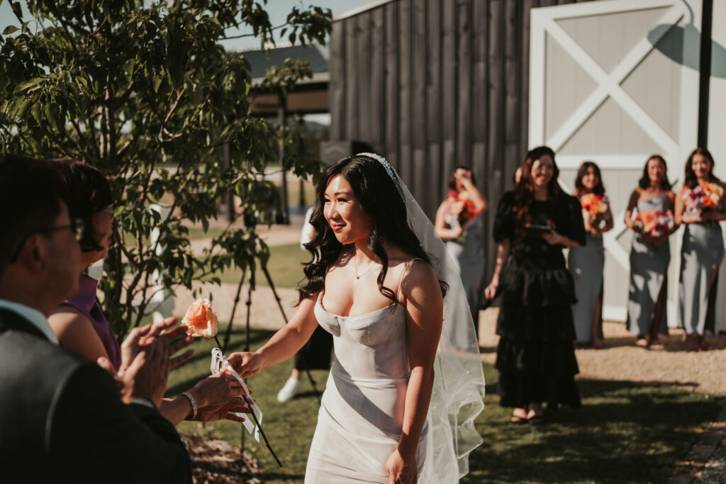 Bride receiving a peach-coloured rose from a wedding guest