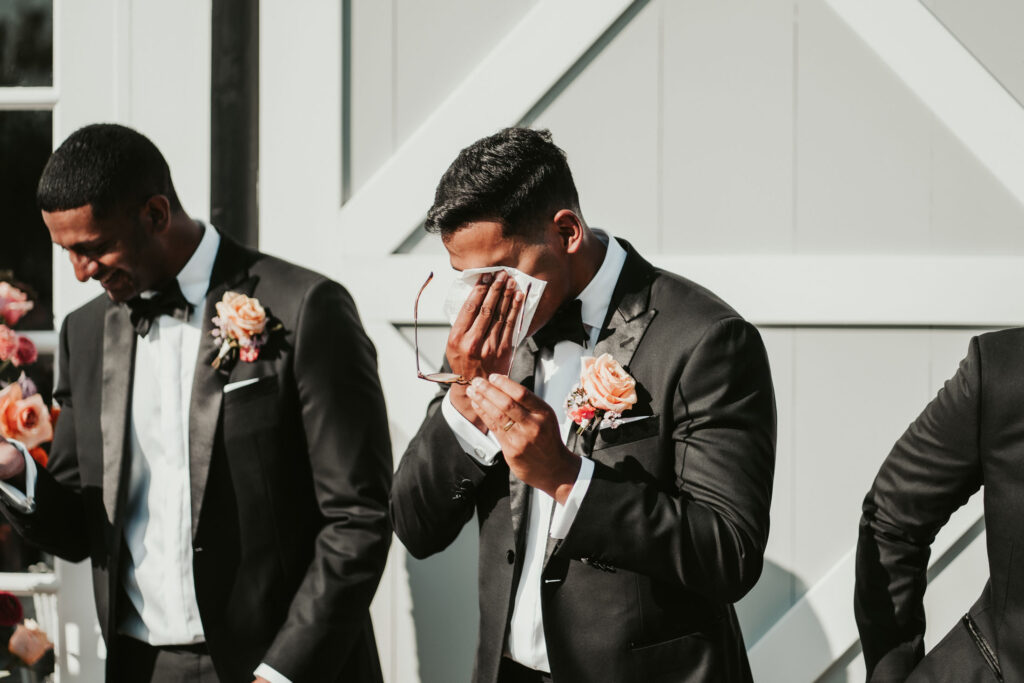 Groomsman crying and dabbing his eye with a handkerchief
