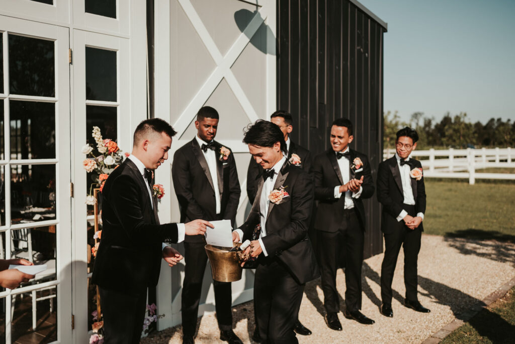 Groom placing a piece of paper in a bucket held up by his groomsman
