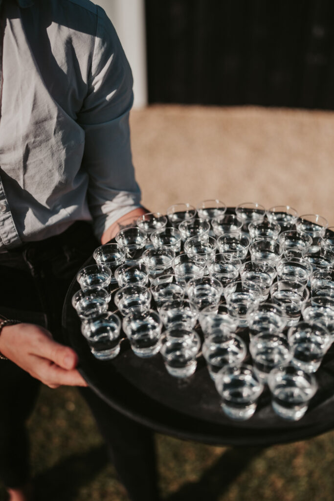 Groomsman holding a tray with dozens of shot glasses with alcohol
