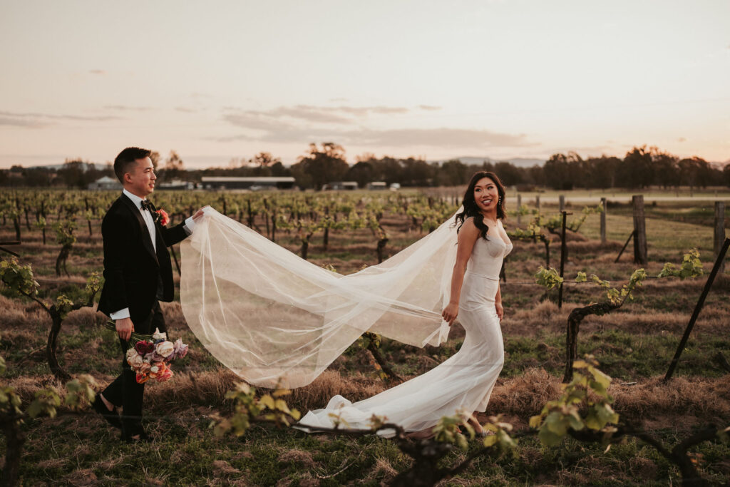 Groom holding up bride's veil as they walk through the vineyard at Dark Horse Vineyard