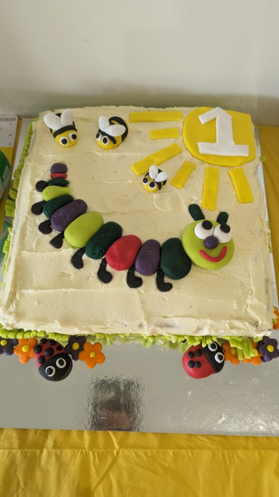 Yellow cake decorated with a large caterpillar, small bees and lady bugs, and a sun with number 1