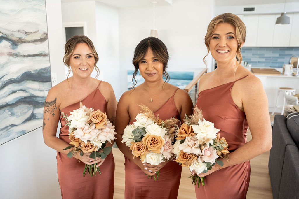 Three bridesmaids smiling while holding their bouquets