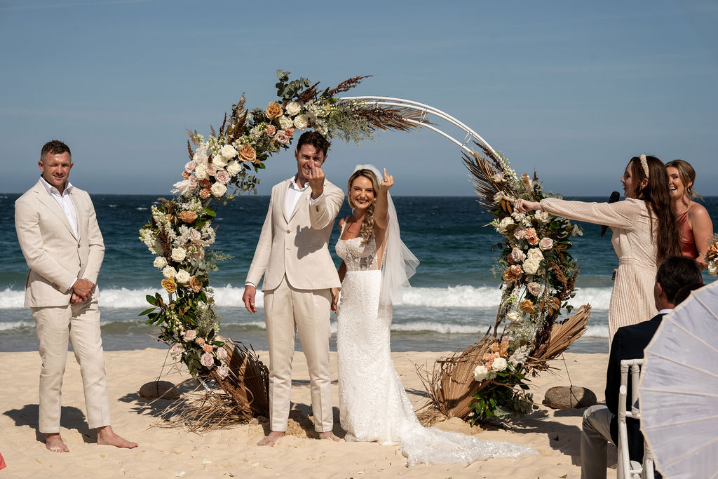 Newlyweds showing off their wedding rings by the sea shore at Zenith Beach