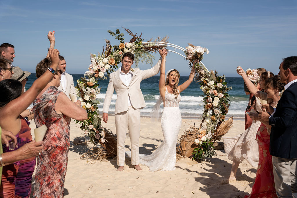 Newlyweds cheering together in front of arbour at Zenith Beach