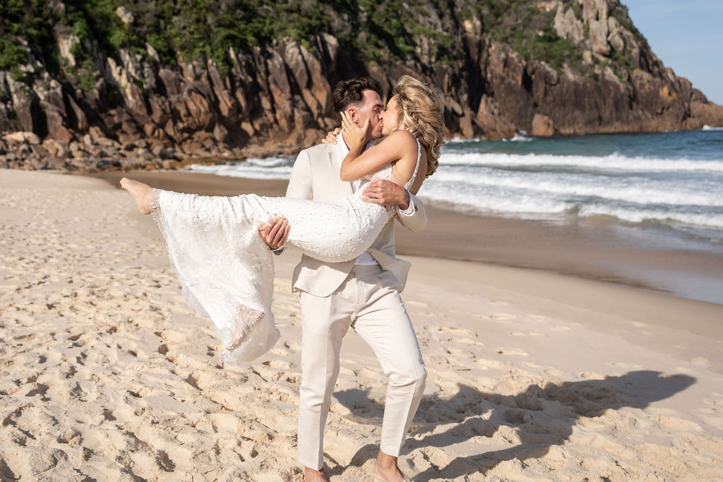 Newlyweds sharing a kiss while husband is princess-carrying his wife at Zenith Beach