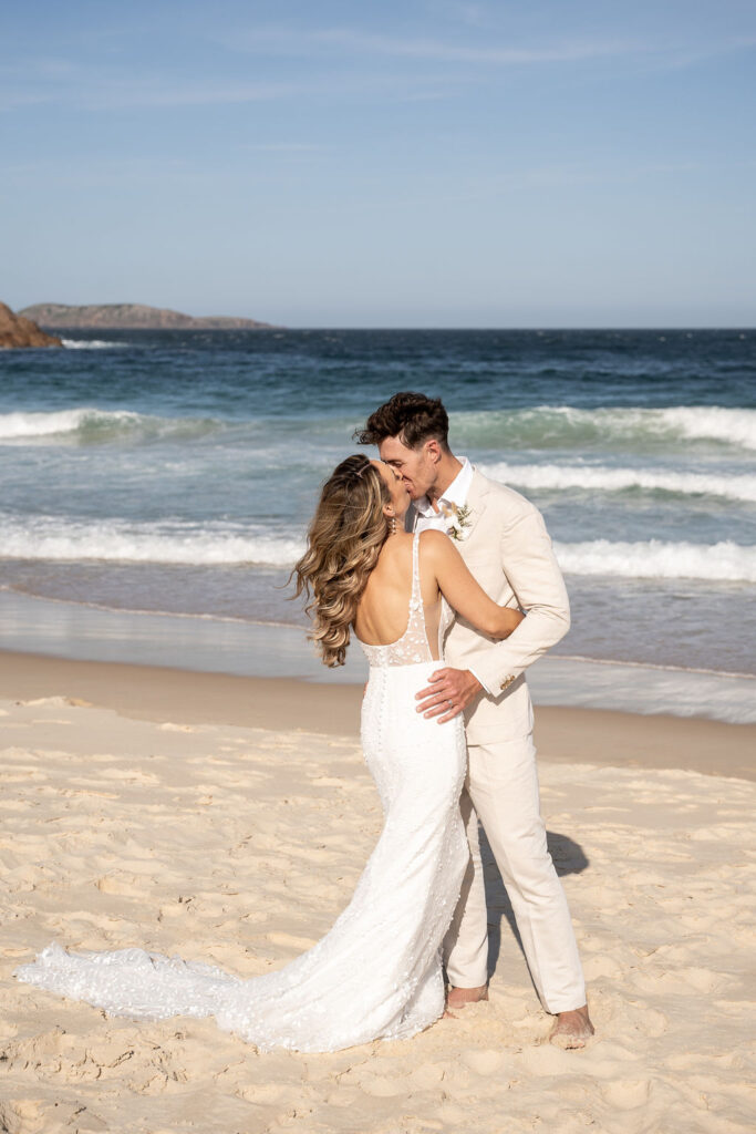 Bride and groom hugging and sharing a kiss by the sea shore