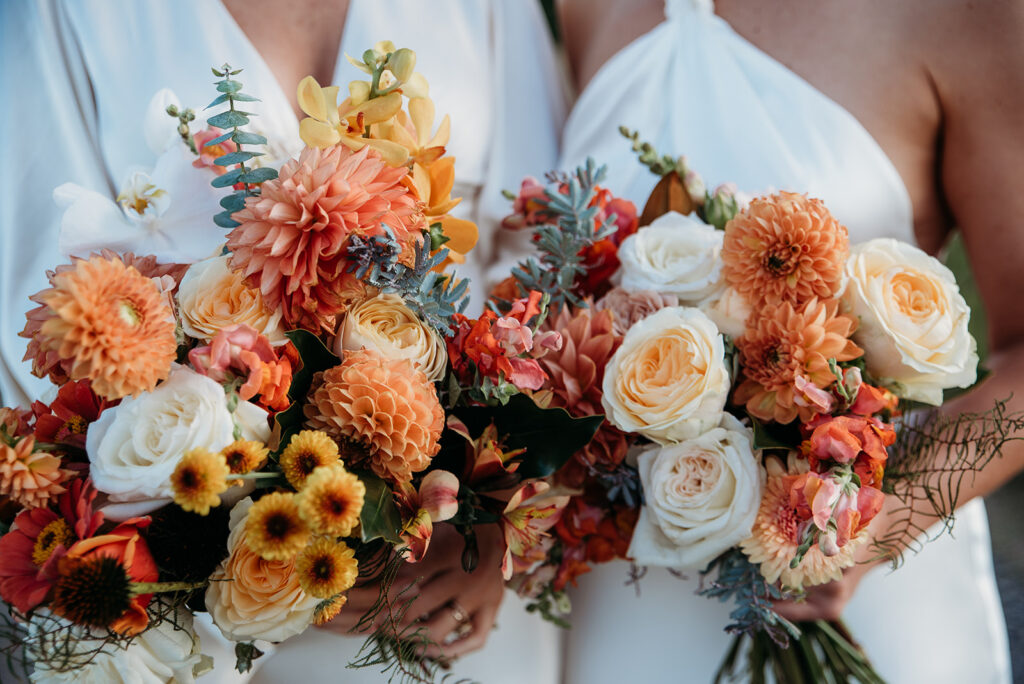 Two brides holding two orange hued bouquets