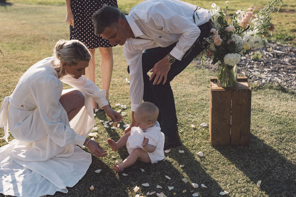 Baby playing on the ground with rose petals during the wedding ceremony of her parents at Wallaringa Farm