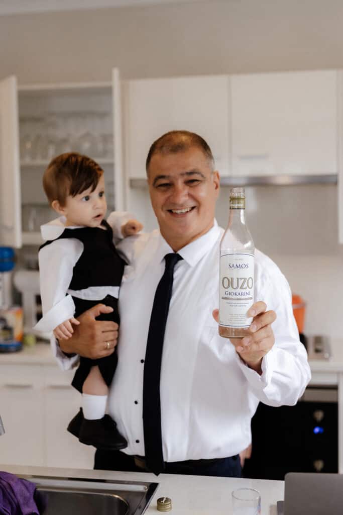 Man holds little boy and bottle of Ouzo morning of wedding at Peterson House Chapel