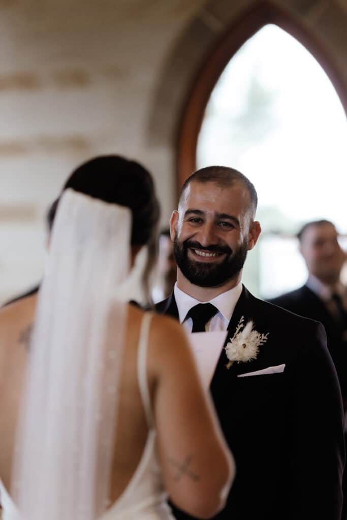 Groom with a huge smile on his face as the bride reads her vows to him at Peterson House Chapel