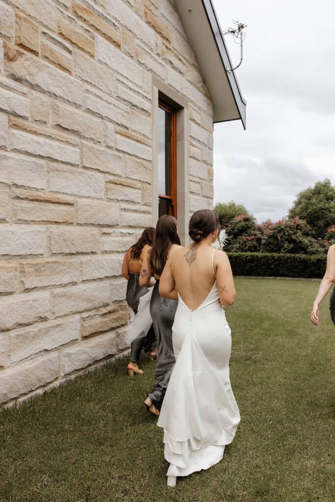 Bride walking around the side of Peterson House Chapel with her bridesmaids