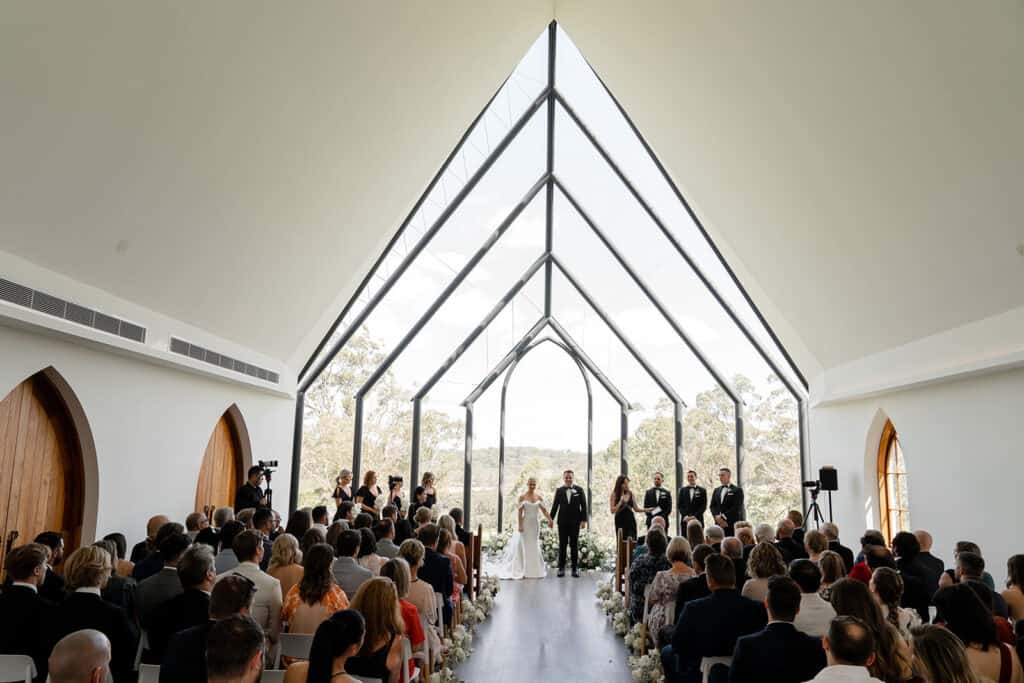 Couple stand in front of huge glass background at Chapel Ridge