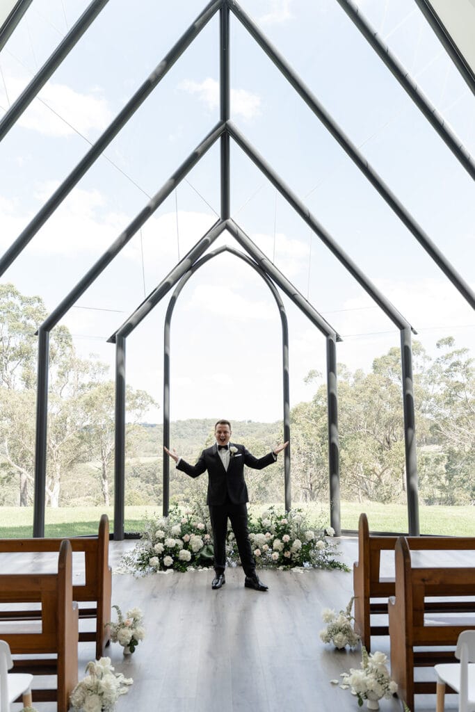 Groom in the centre of the aisle surrounded by flowers at Chapel Ridge