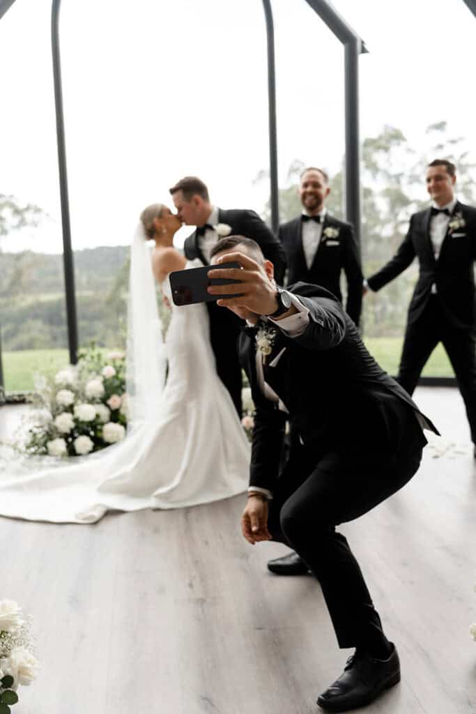 Groomsman with a camera taking a selfie with the couple
