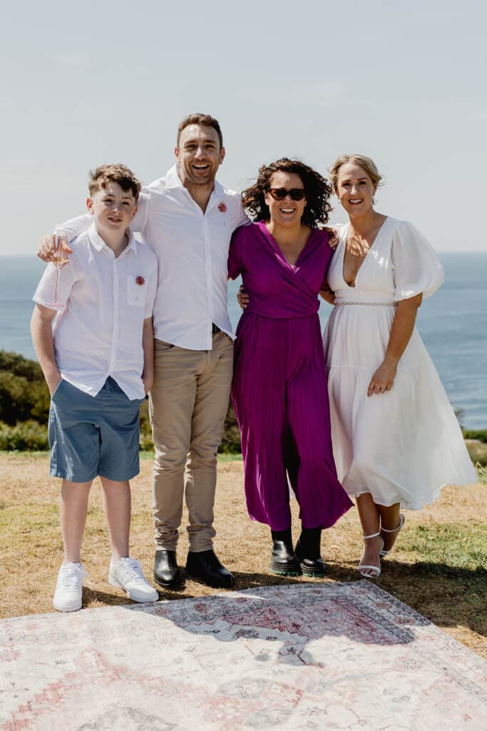 Photographer Dea from Little Black Bow Photography standing with couple and son after  Newcastle coastal wedding