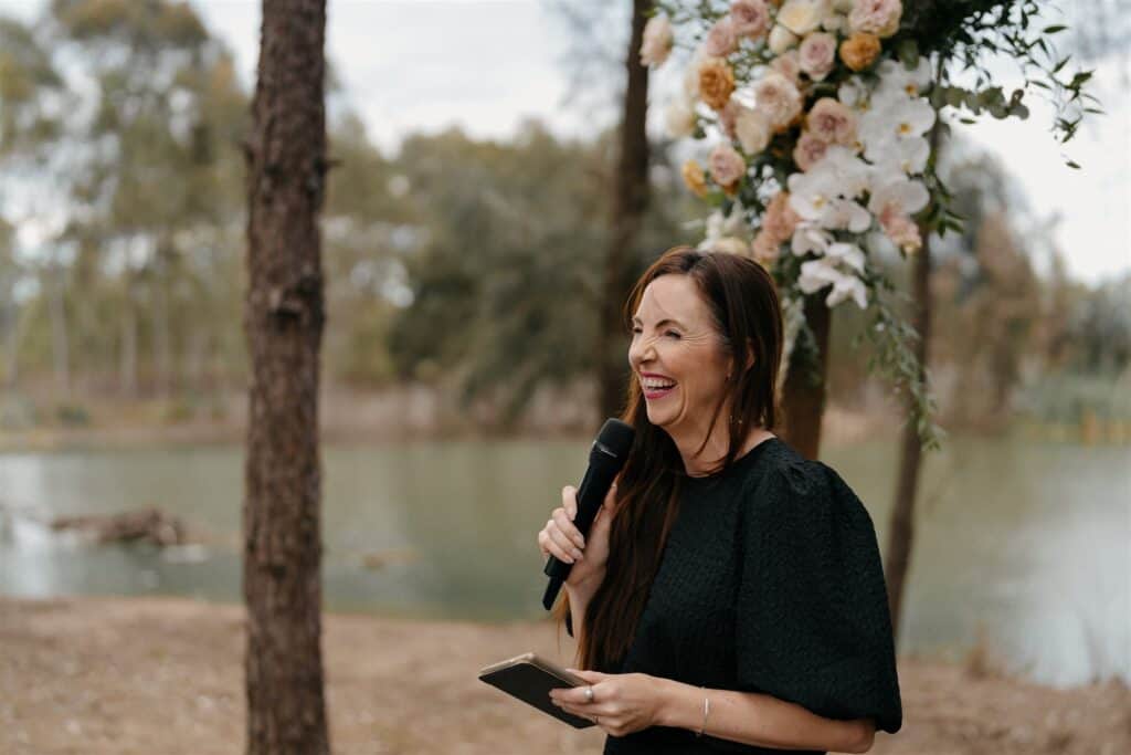 Celebrant Julie Muir holding a mic and Kindle during wedding ceremony at The Wine House