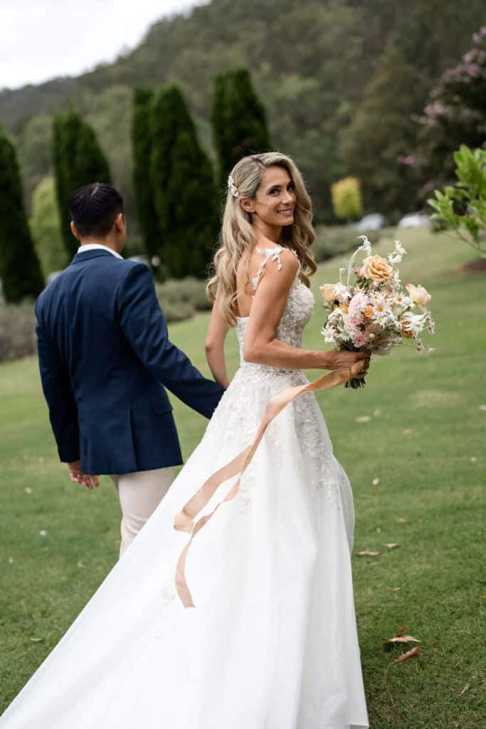 Couple walking across the lawn at Redleaf Wollombi, bride holding bouquet