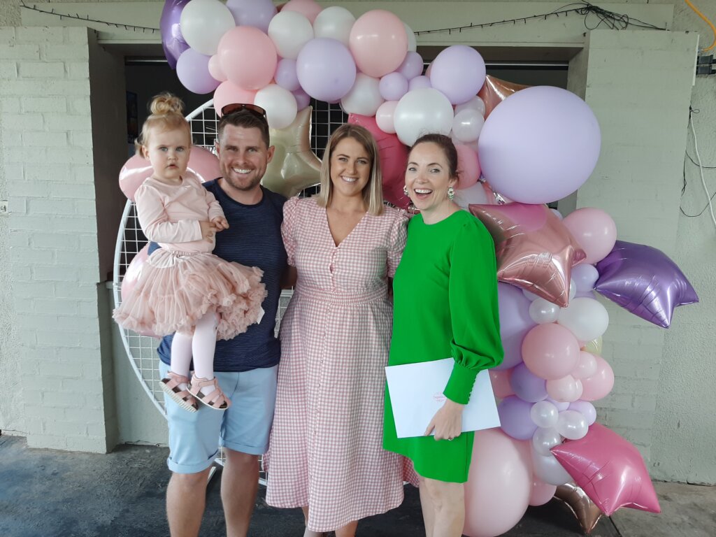 julie-muir-with-the-mom-and-dad-during-the-non-religious-christening-ceremony-with-pink-balloons-in-the-background